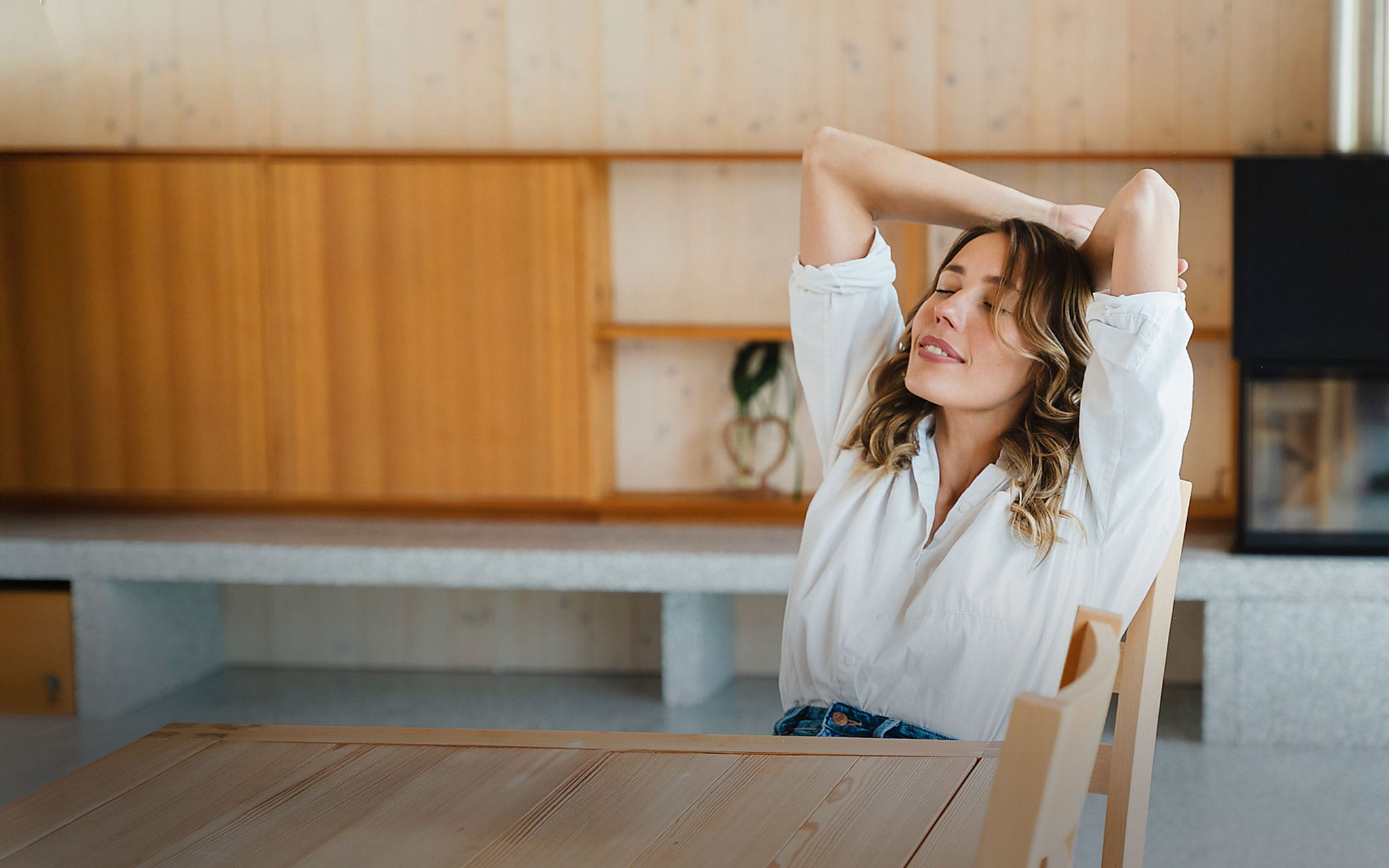 Eine Frau sitzt entspannt am Tisch in einer minimalistisch eingerichteten Wohnung