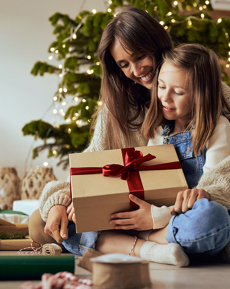 Mutter und Tochter vor dem Weihnachtsbaum packen Geschenke aus