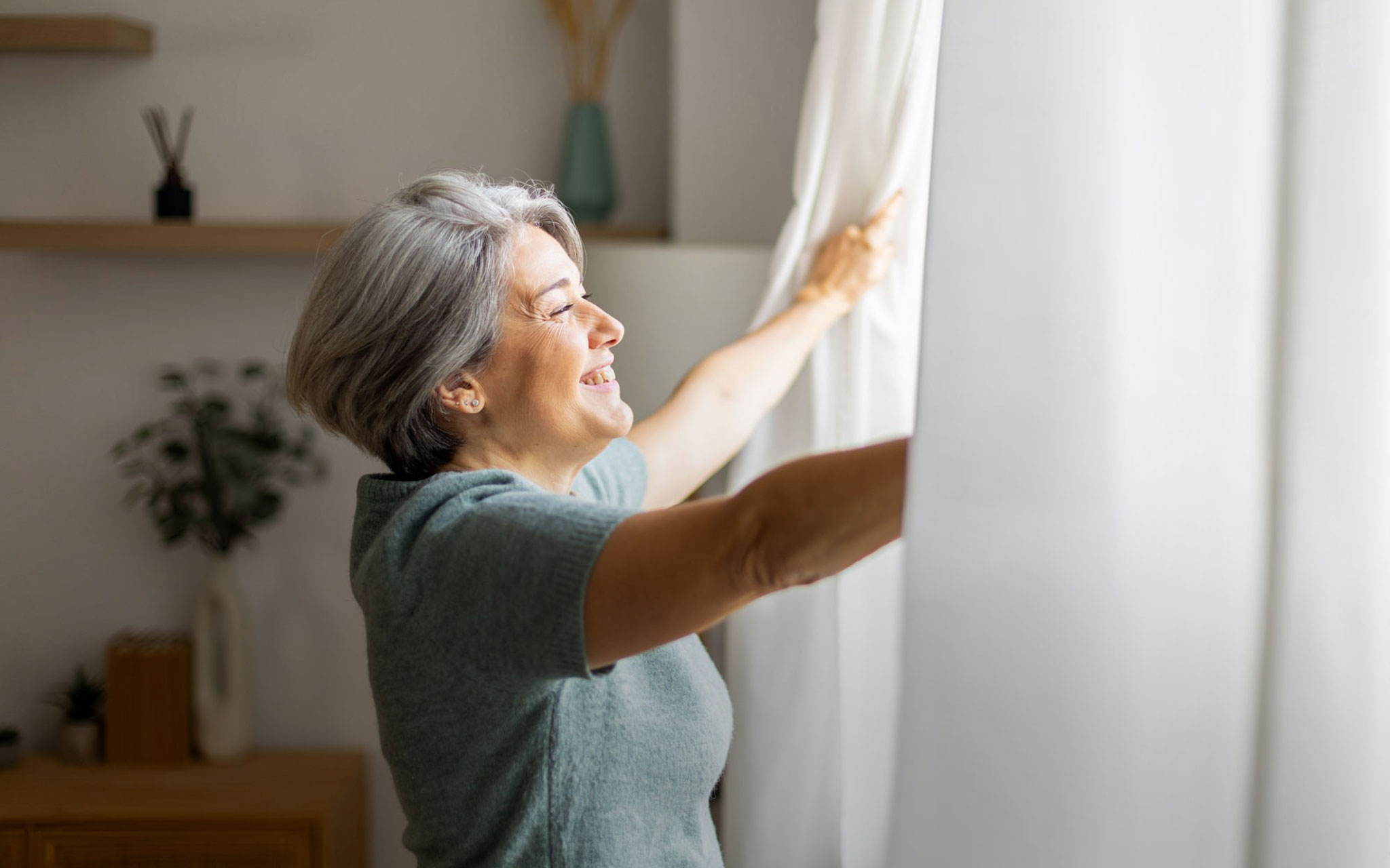 Die Vorhänge vor einem Fenster werden von einer fröhlichen Frau geöffnet