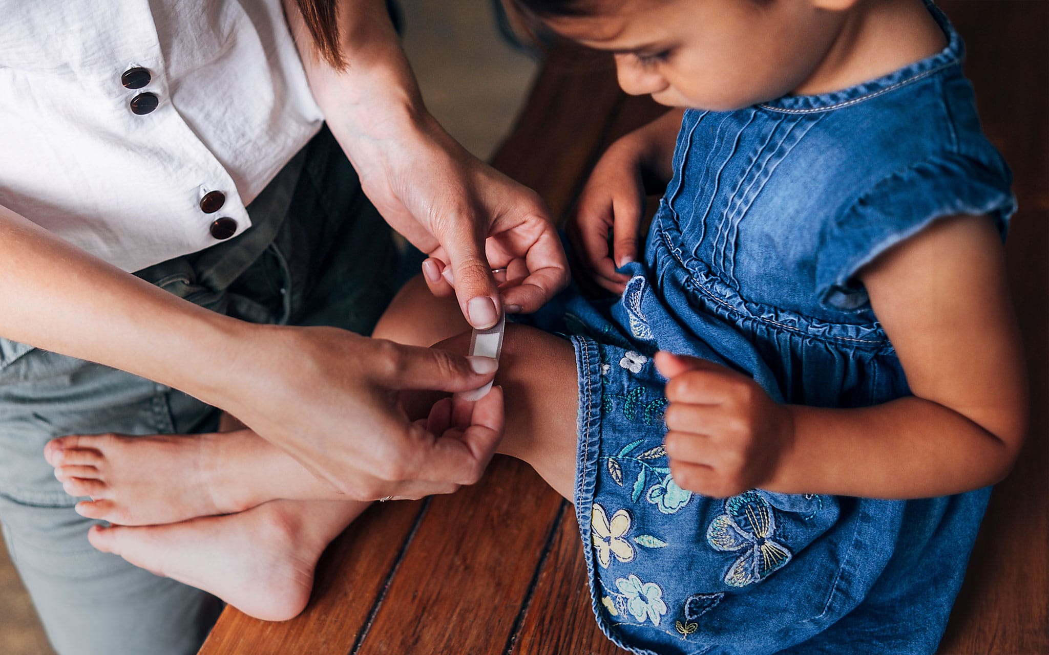 Mutter klebt Pflaster auf das Knie der kleinen Tochter