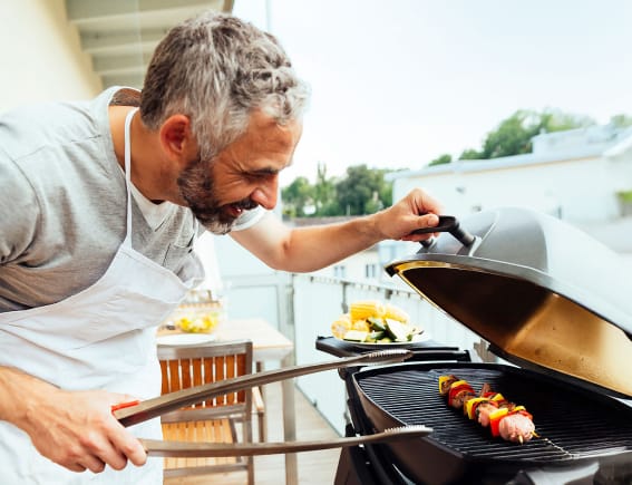 Mann auf Balkon schaut auf seinen Grill
