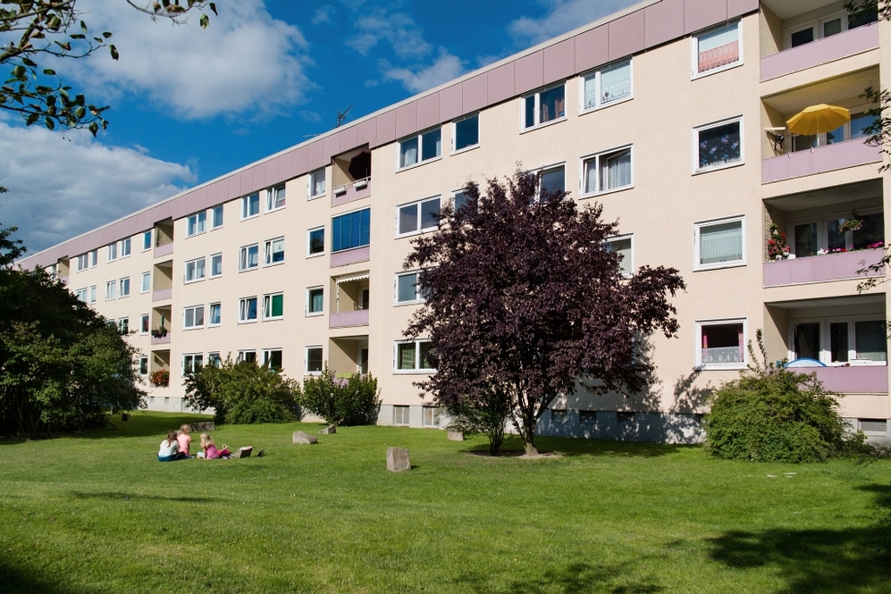 Mehrstöckiges Wohngebäude mit Balkon, grünem Rasen und drei Personen auf der Wiese.
