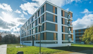 Modernes Wohngebäude mit großen Fenstern und Grünfläche bei Sonnenschein.
