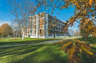 Moderner Wohnkomplex mit Park und herbstlichen Bäumen bei klarem Himmel.