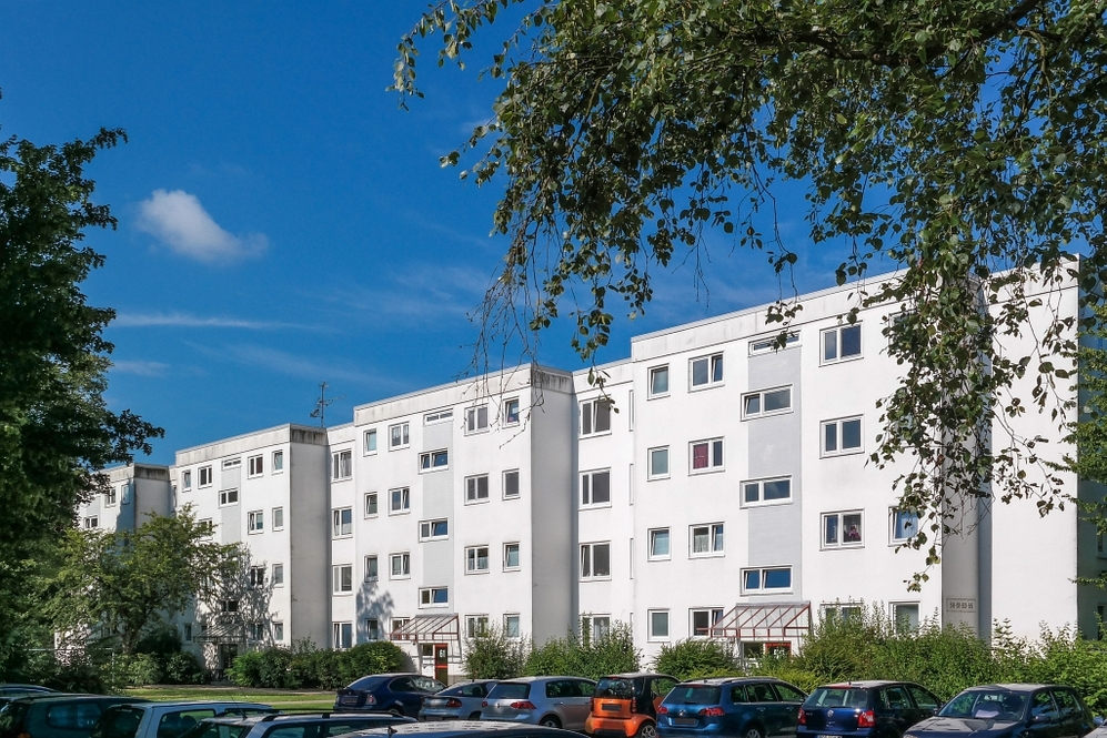 Mehrstöckige weiße Wohngebäude mit Parkplätzen und Bäumen bei klarem Himmel.