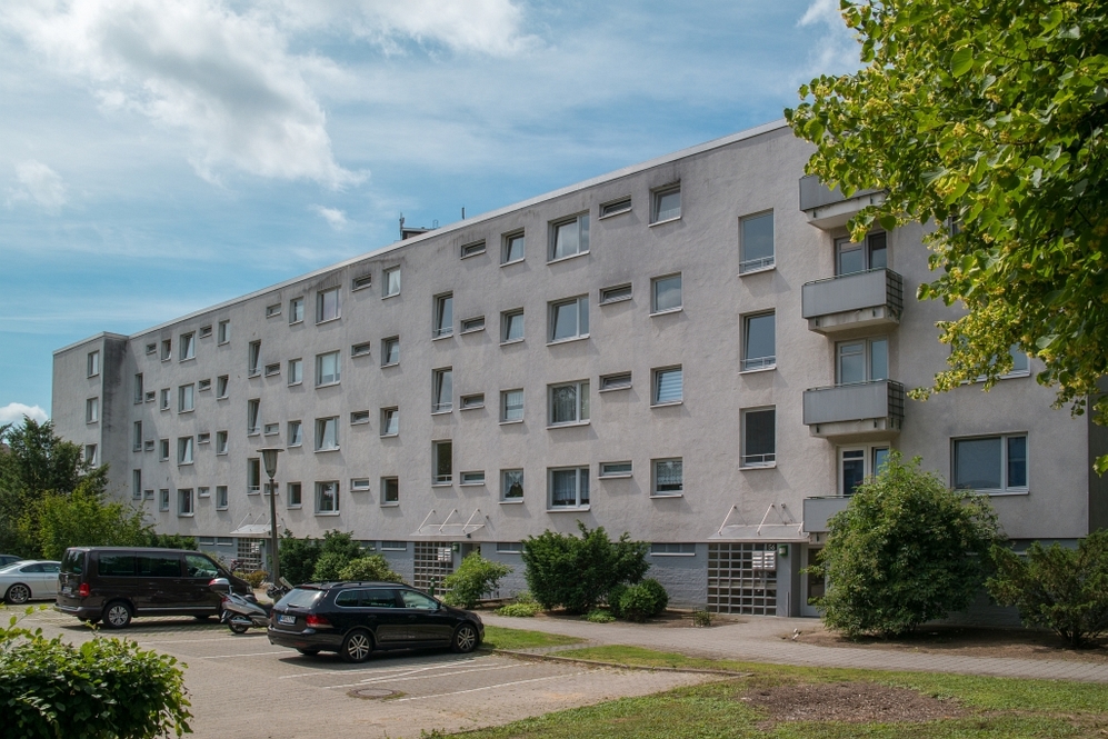Mehrstöckiges Wohngebäude mit Parkplätzen und Grünflächen im Vordergrund.