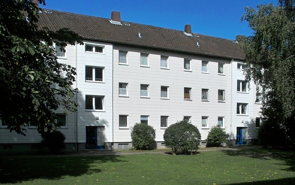 Mehrfamilienhaus mit weißer Fassade, blauen Türen und Grünfläche im Vordergrund.
