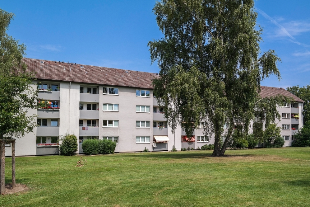 Mehrfamilienhaus mit Balkonen, großem Rasen und Bäumen bei klarem Himmel.