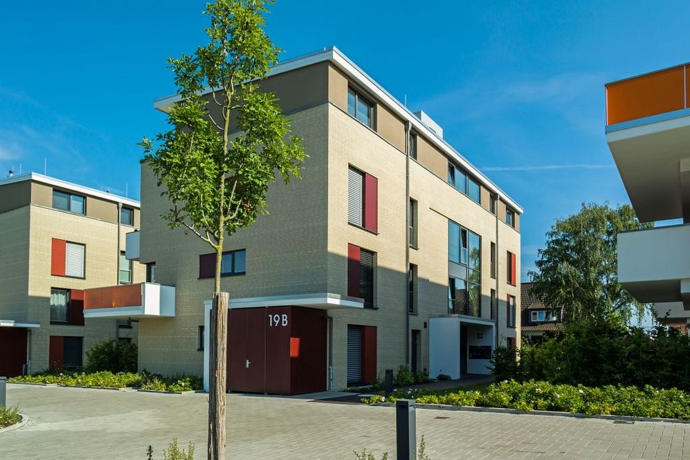 Moderne Wohnanlage mit drei- bis vierstöckigen Gebäuden und begrünten Außenanlagen bei klarem Himmel.