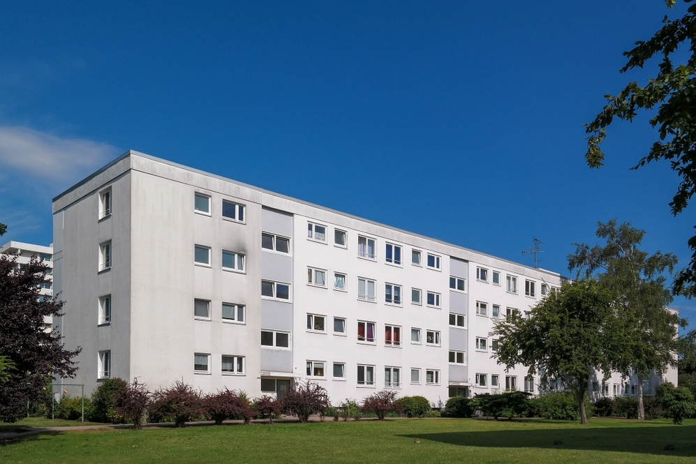 Mehrgeschossiges Wohngebäude mit weißen Fassaden und Grünfläche bei klarem Himmel.