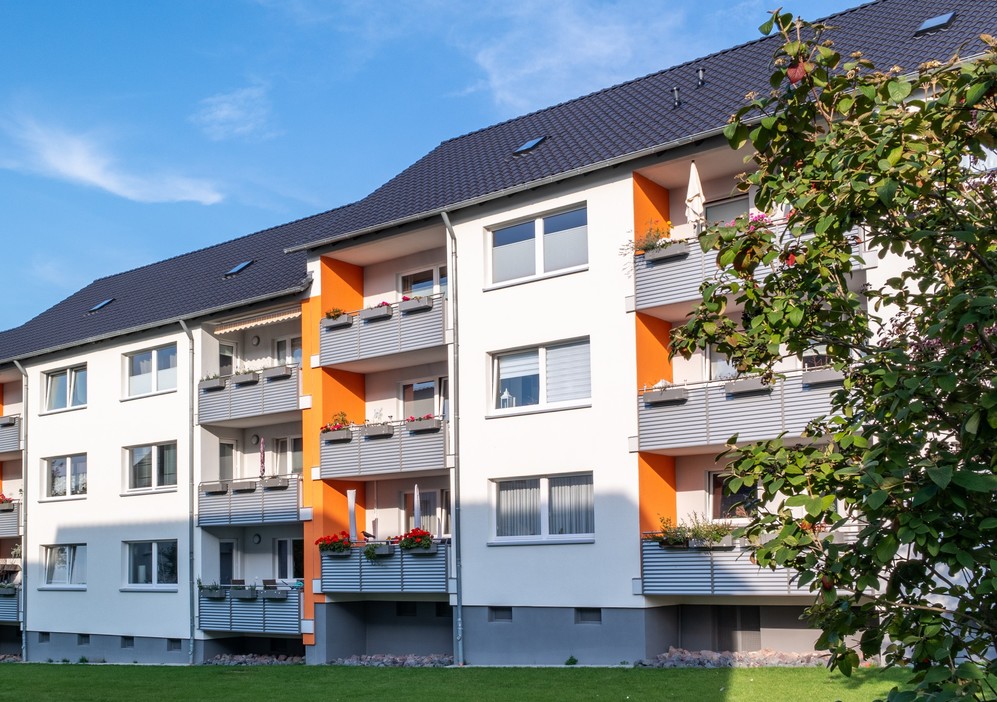 Moderne Wohnanlage mit weißen Fassaden, orangen Akzenten und Balkonen, grüner Rasen im Vordergrund.