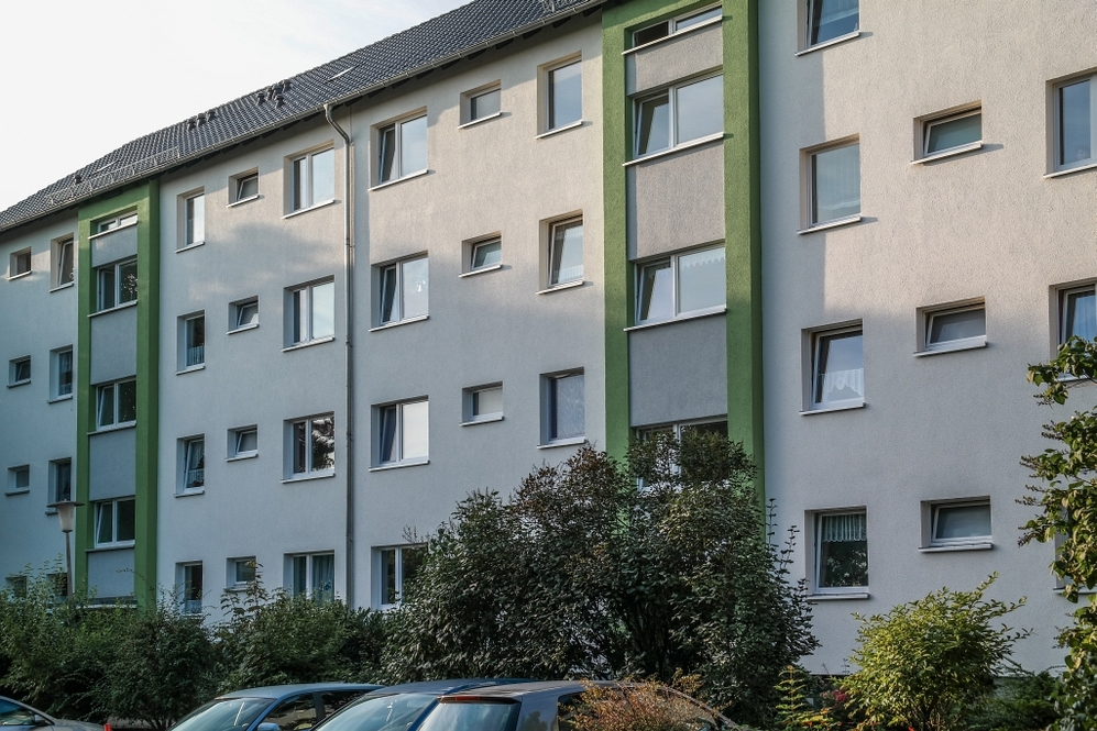 Mehrstöckiges Wohngebäude mit weißen Fassaden und grünen Akzenten, davor parkende Autos.