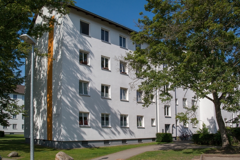 Mehrstöckiges Wohngebäude mit weißer Fassade, umgeben von Bäumen und Grünflächen.
