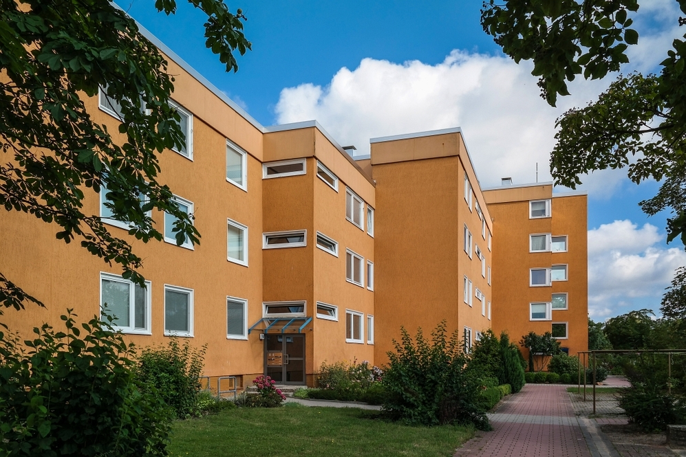 Mehrgeschossiges Wohngebäude mit orangefarbener Fassade und umliegender Grünanlage bei blauem Himmel.