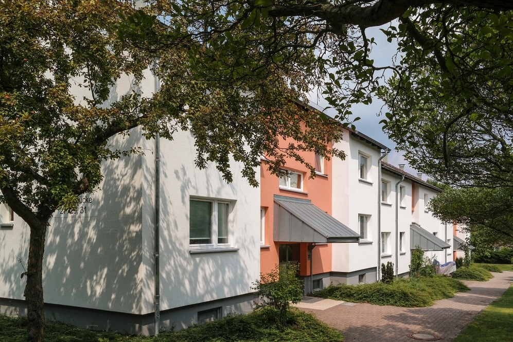 Mehrfamilienhaus mit weiß-oranger Fassade, begrüntem Vorgarten und Bäumen im Wohngebiet.