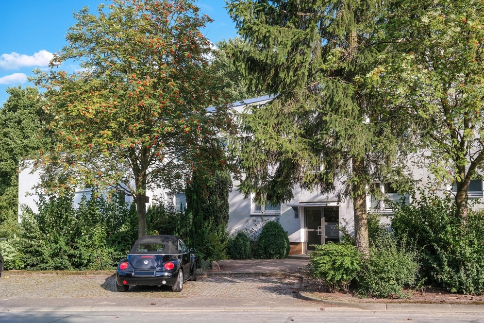 Mehrfamilienhaus mit begrüntem Vorgarten und Stellplatz mit kleinem schwarzem Auto.