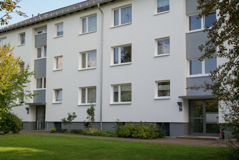 Mehrfamilienhaus mit weißer Fassade, mehreren Fenstern und gepflegtem Vorgarten.