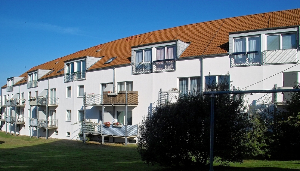 Mehrgeschossige Wohnanlage mit weißen Fassaden, Balkonen und roten Ziegeldächern bei Sonnenschein.