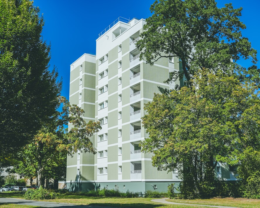 Mehrstöckiges Wohngebäude in grüner Umgebung mit blauen Himmel im Hintergrund.
