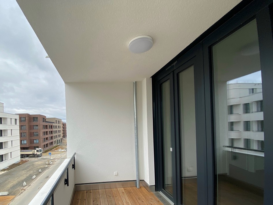 Balkon mit Holzboden und Glasgeländer an Neubauwohnung in moderner Wohnanlage.