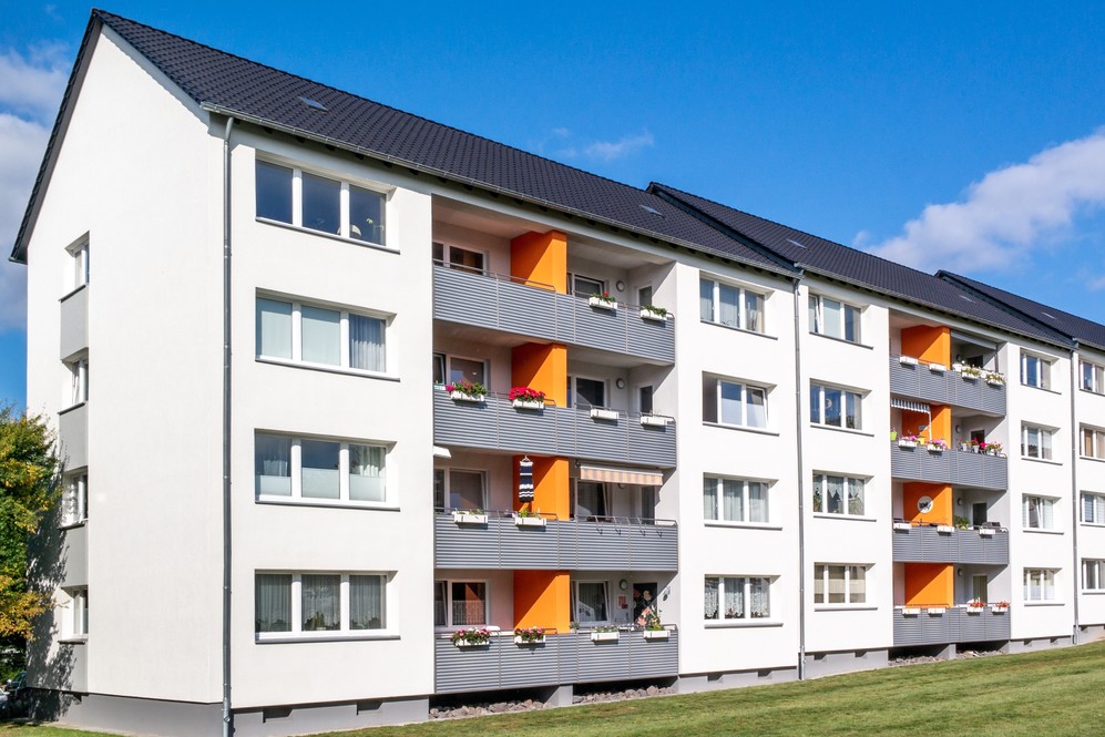 Mehrgeschossige Wohnanlage mit weißen Fassaden und orangefarbenen Balkonelementen bei Sonnenschein.