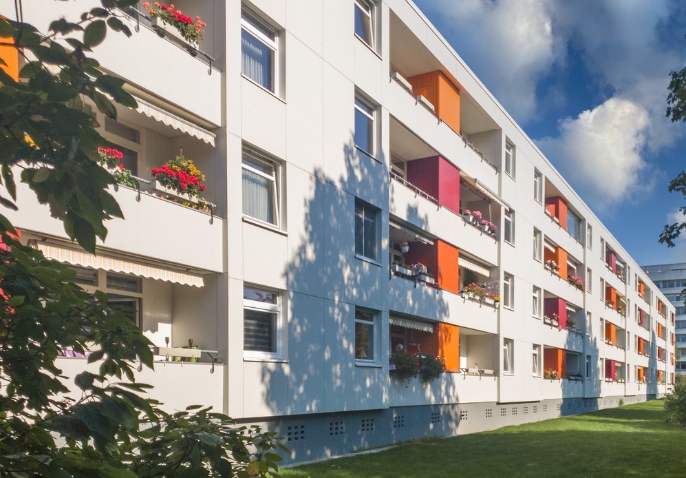 Mehrstöckiges Wohngebäude mit farbigen Balkons und Blumen unter blauem Himmel.