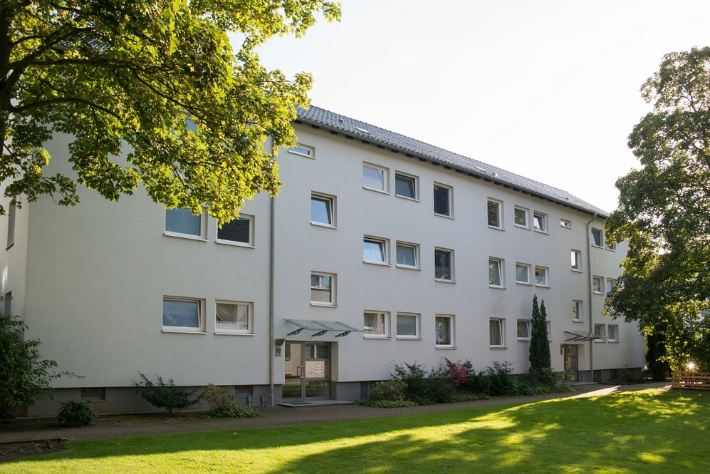 Mehrstöckiges Wohngebäude mit weißen Fassaden und Grünfläche im Vordergrund.