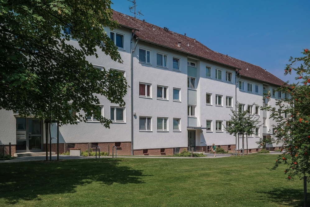Mehrgeschossige Wohnhäuser mit weißer Fassade, Dachziegeln und Grünfläche im Vordergrund.