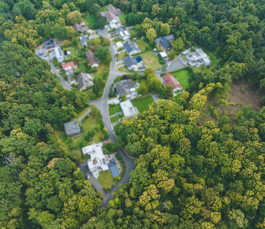 Wohnsiedlung mit Einfamilienhäusern umgeben von dichtem Wald aus der Vogelperspektive.