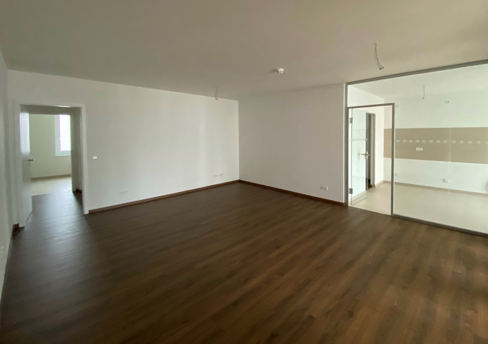 Leeres Wohnraum mit dunklem Holzboden, weiß gestrichenen Wänden und Zugang zu angrenzendem Raum.