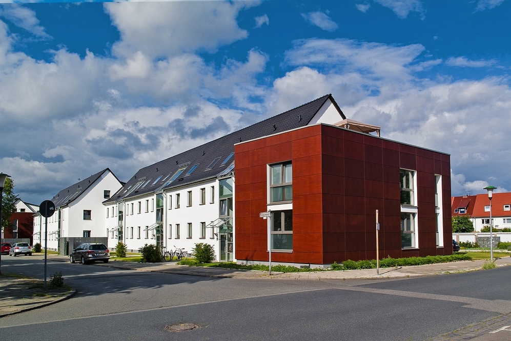 Moderne Wohnanlage mit weißem Haupthaus und rotem Anbau an ruhiger Straßenecke.