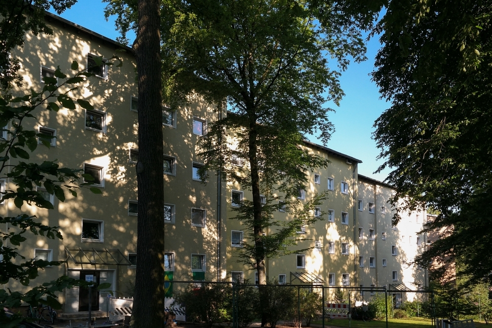 Mehrgeschossiges Wohngebäude mit gelber Fassade umgeben von Bäumen und Grünfläche.