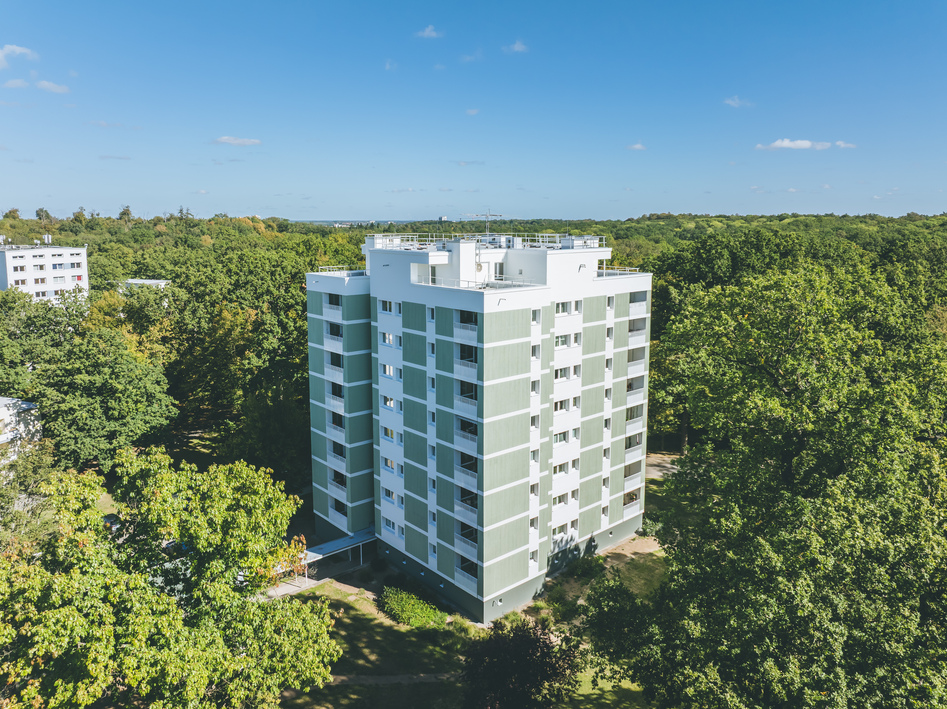 Mehrstöckiges Wohngebäude umgeben von dichtem Grün unter klarem blauem Himmel.