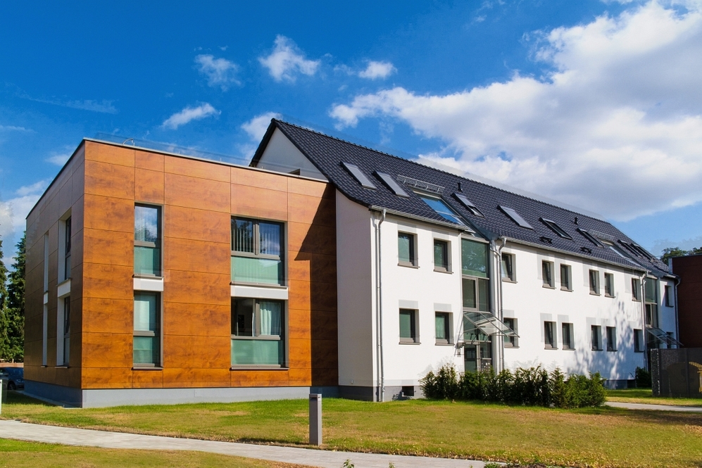 Modernes Mehrfamilienhaus mit Holzfassade und weißen Wänden unter blauem Himmel.