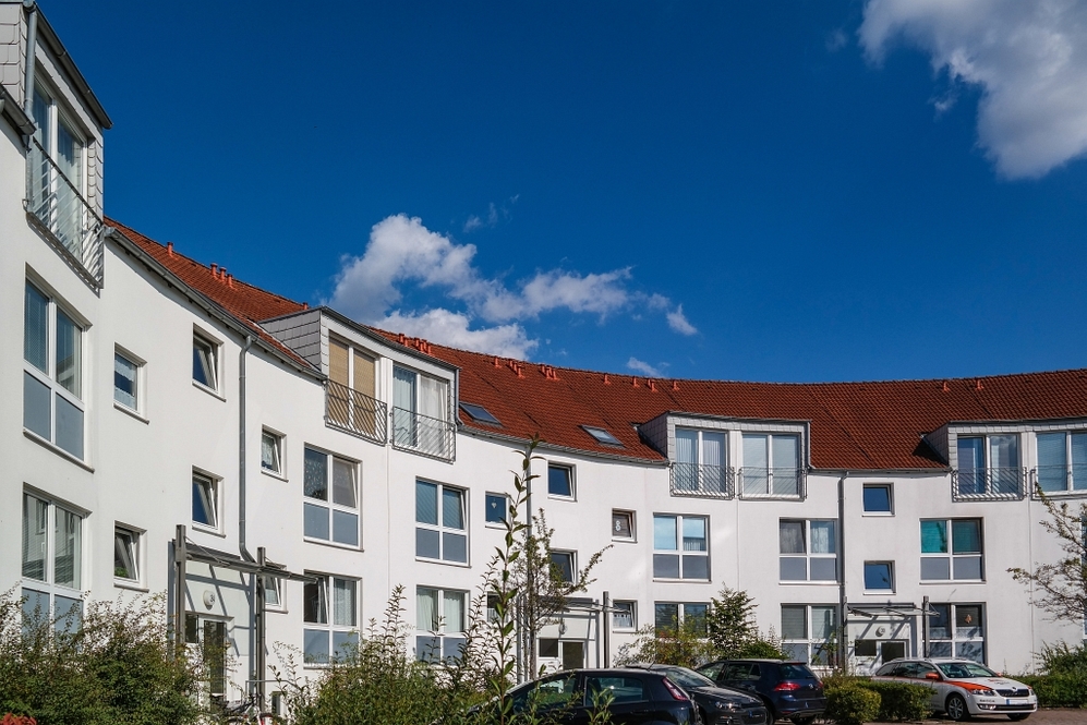 Moderne, gebogene Wohnhausanlage mit weißen Fassaden und roten Ziegeldächern unter blauem Himmel.
