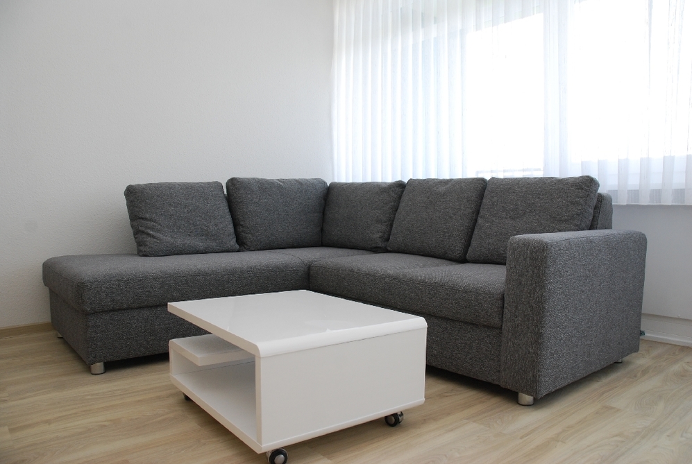 Graues Ecksofa mit weißem, rollbarem Couchtisch in modernem, hellem Wohnzimmer.