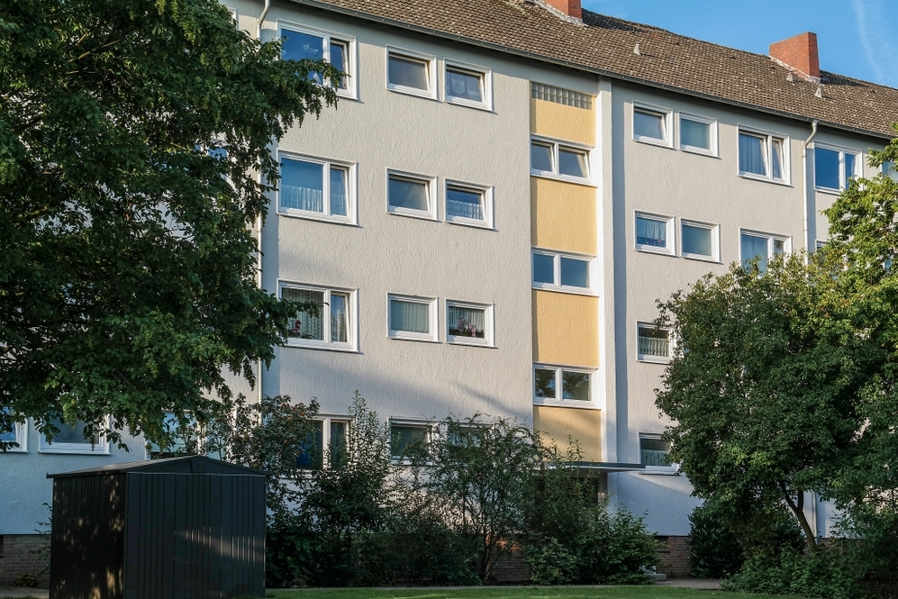 Mehrgeschossiges Wohngebäude mit weißen Fassaden und gelben Akzenten, umgeben von Bäumen.