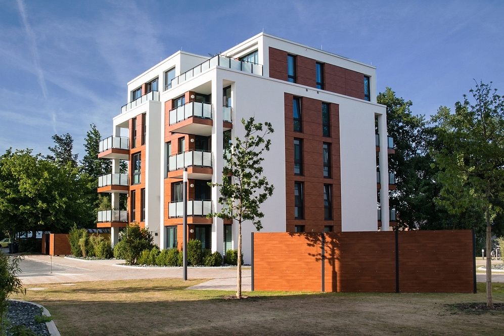 Modernes Mehrfamilienhaus mit Balkonen und Holzfassade, umgeben von Grünflächen.