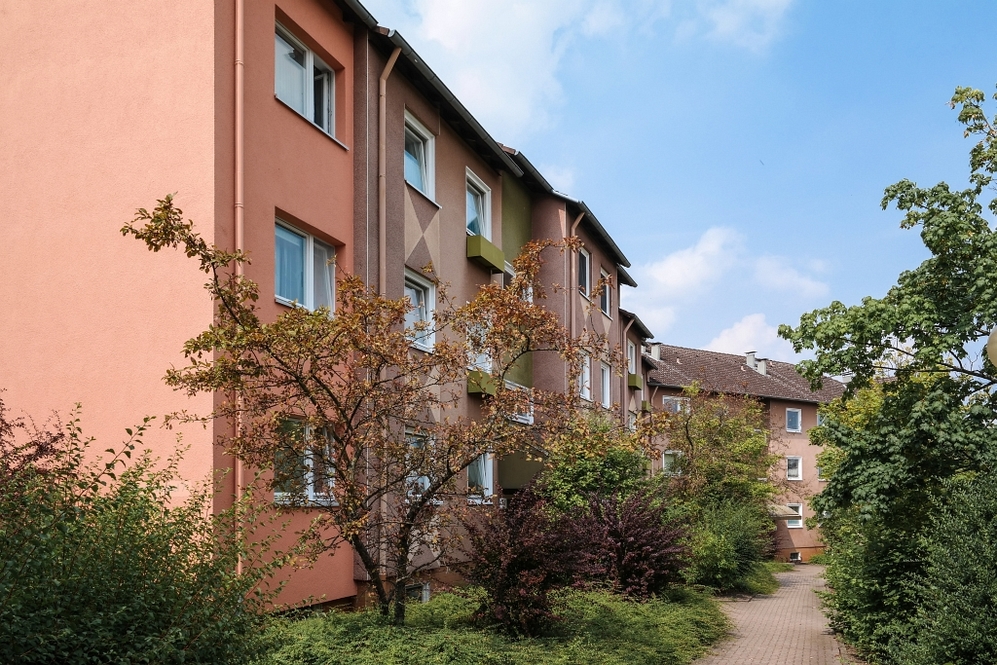 Mehrstöckige Wohngebäude mit bunten Fassaden und grüner Bepflanzung an einem Gehweg.