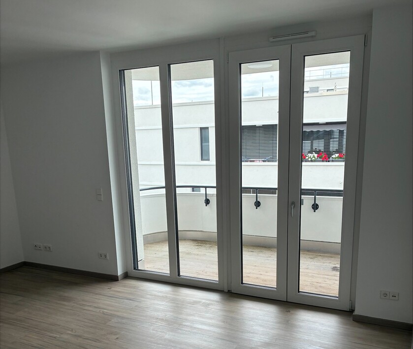 Leere Wohnraumwohnung mit Holzfußboden und großen Fenstertüren zum Balkon.