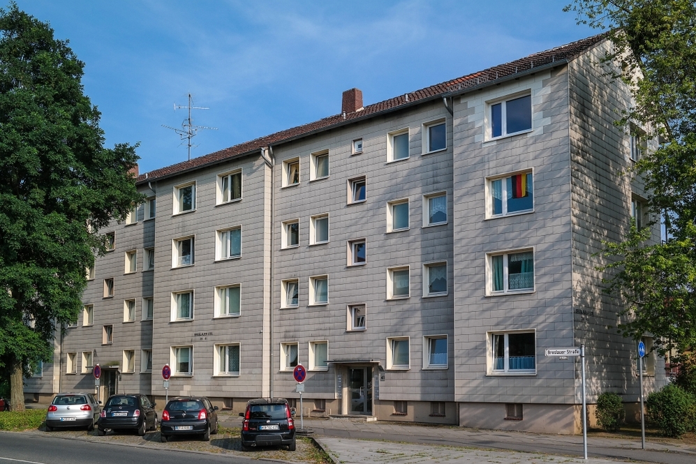 Mehrfamilienwohnhaus mit grauer Fassade, Parkplätzen und Bäumen an der Straße.