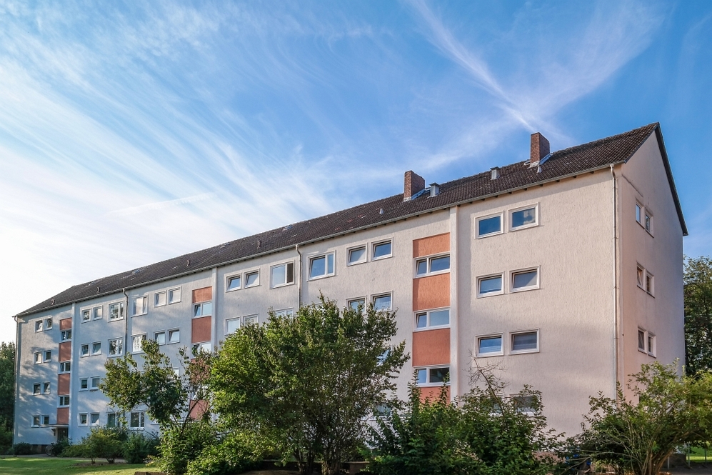 Mehrstöckiges Wohngebäude mit weißen und orangen Fassadenabschnitten, umgeben von Grünfläche.