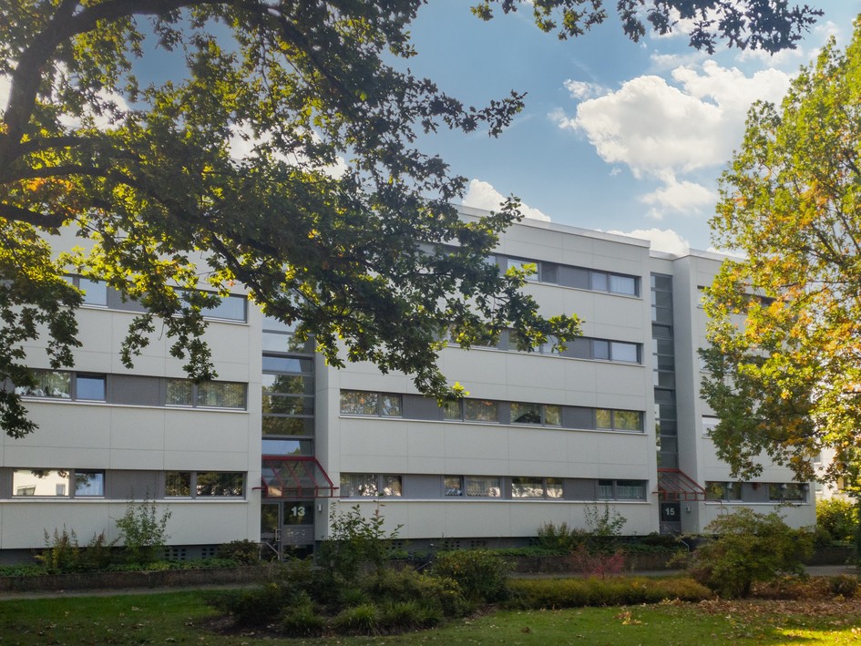 Moderne Wohngebäude mit großen Fenstern, umgeben von Bäumen und Grünflächen.
