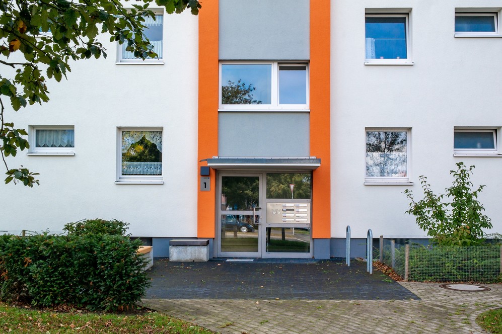 Mehrfamilienhaus mit orangefarbener Fassadensäule und Glas-Hauseingangstür.