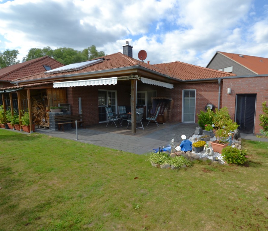 Einfamilienhaus mit überdachter Terrasse, Garten und kleiner bepflanzter Sitzecke.