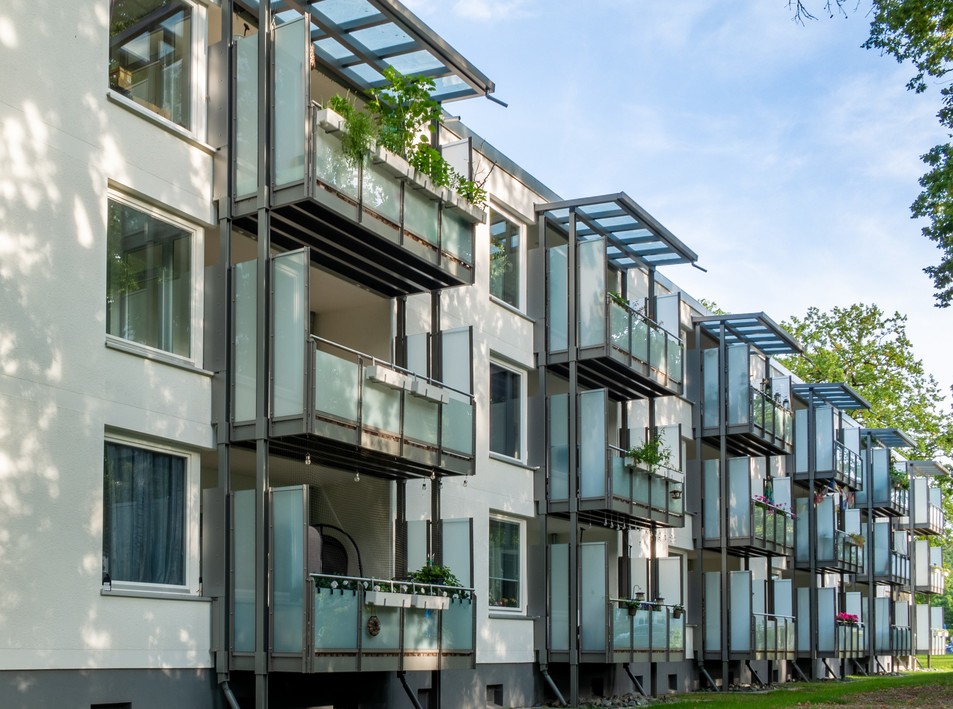 Mehrstöckiges Wohngebäude mit modernen Balkonen und Pflanzen, umgeben von Grünflächen.