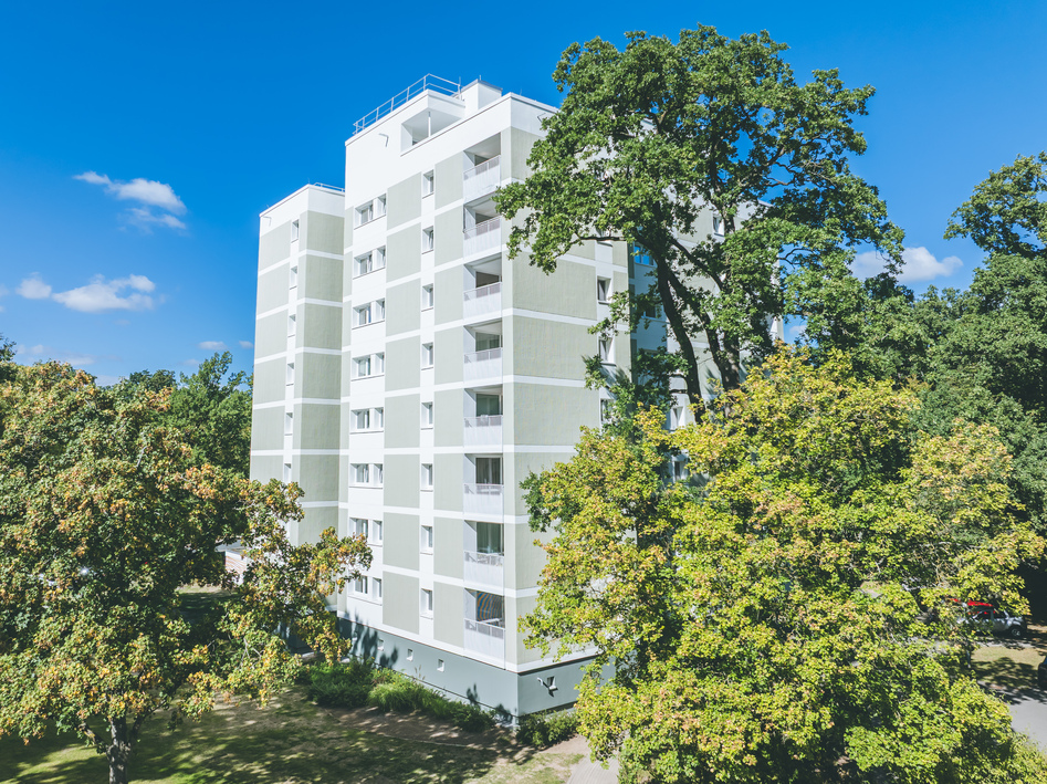 Mehrstöckiges Wohngebäude umgeben von Bäumen unter blauem Himmel.