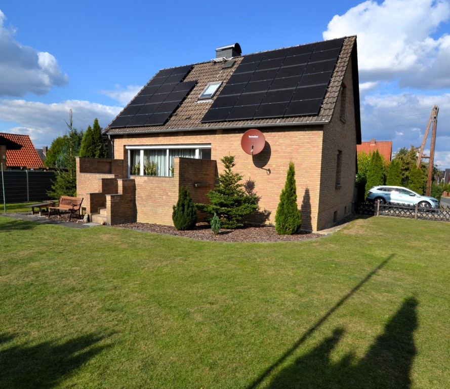 Einfamilienhaus mit Solarpanelen auf dem Dach und gepflegtem Garten bei Sonnenschein.