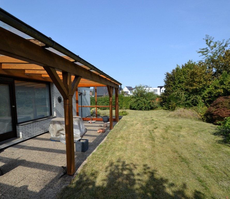 Garten mit überdachter Terrasse an Einfamilienhaus, umgeben von Grün und Nachbarhäusern.