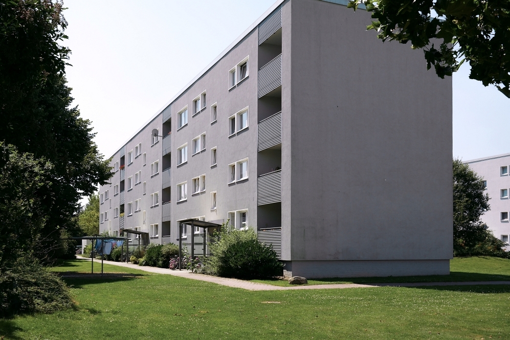 Mehrstöckiges Wohngebäude mit Balkonen, umgeben von Grünflächen und Bäumen.